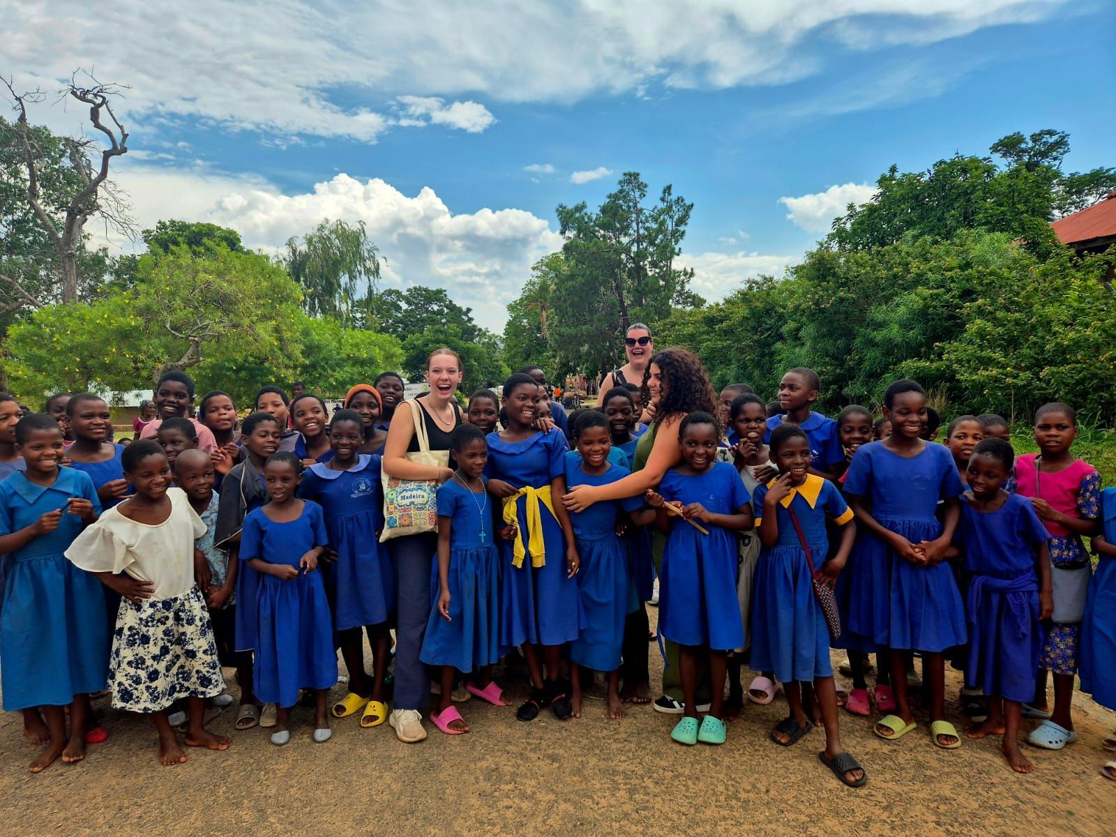 Leerlingen in blauwe schooluniformen samen met studenten van Together for Malawi op een schoolplein in Malawi