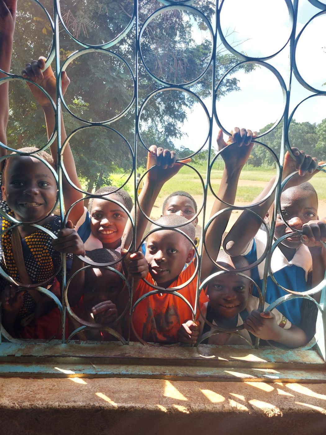 Lachende leerlingen kijken door het raam van een klaslokaal in Malawi
